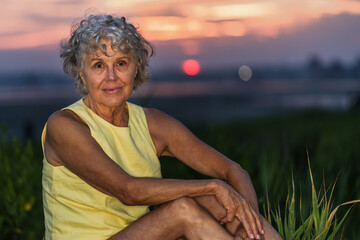 A woman in a yellow tank top is sitting on the grass