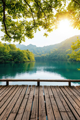 Poster - Serene lakeside view with a wooden deck surrounded by lush greenery and mountains under the warm glow of the setting sun.