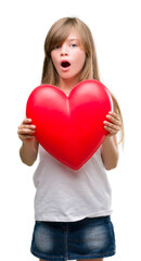 Sticker - Young blonde toddler holding a red heart scared in shock with a surprise face, afraid and excited with fear expression