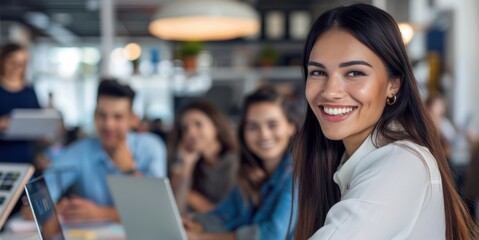 A smiling, happy businesswoman radiates warmth and positivity in the modern office environment, surrounded by her team.