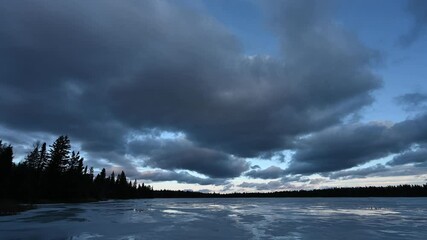 Wall Mural - time lapse of grey and blue colored clouds moving above a frozen lake that has small puddles on top 