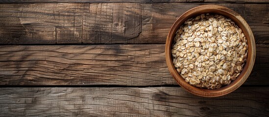 Poster - Top down view of wooden bowl filled with rolled oats on wooden table with rustic background suitable as a copy space image