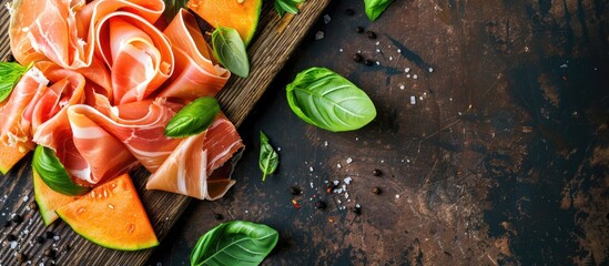 Canvas Print - A top down view of an Italian appetizer prosciutto ham paired with cantaloupe and basil on a wooden board against a rustic dark backdrop with space for text and imagery. Copy space image