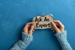 © Jullia - Expert Consulting Concept with Hands Holding 'Ask An Expert' Sign on Blue Background