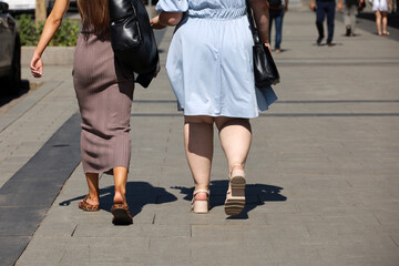 Fat and slim women walking down the street, back view. Female fashion in summer city