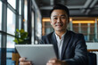 © john - happy asian mid age business man professional ceo using tablet computer, looking at camera at desk in the office