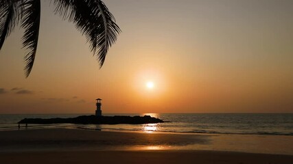 Wall Mural - sunset over khao lak beach with lighthouse and coconut palm tree silhouette. tranquil coastal scene 