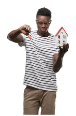 Wall Mural - Young african american man holding house with angry face, negative sign showing dislike with thumbs down, rejection concept