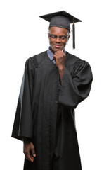 Canvas Print - Young graduated african american man over isolated background with hand on chin thinking about question, pensive expression. Smiling with thoughtful face. Doubt concept.