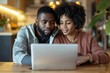 © Yuliia - Close-up photo of a young African American couple shopping online together on a laptop in the comfort of their own home.