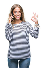 Wall Mural - Beautiful young blonde woman talking on smarpthone over isolated background doing ok sign with fingers, excellent symbol