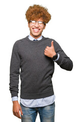 Canvas Print - Young handsome business man with afro hair wearing glasses doing happy thumbs up gesture with hand. Approving expression looking at the camera with showing success.