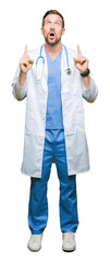 Wall Mural - Handsome doctor man wearing medical uniform over isolated background amazed and surprised looking up and pointing with fingers and raised arms.