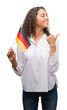 © Krakenimages.com - Young hispanic woman holding flag of Germany pointing and showing with thumb up to the side with happy face smiling