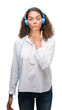 © Krakenimages.com - Young hispanic woman wearing headphones cover mouth with hand shocked with shame for mistake, expression of fear, scared in silence, secret concept