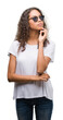 © Krakenimages.com - Young hispanic woman wearing sunglasses with hand on chin thinking about question, pensive expression. Smiling with thoughtful face. Doubt concept.