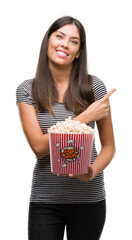 Sticker - Young beautiful hispanic eating popcorn very happy pointing with hand and finger to the side