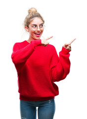 Young beautiful blonde woman wearing red sweater and glasses over isolated background smiling and looking at the camera pointing with two hands and fingers to the side.