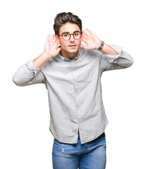 Wall Mural - Young handsome man wearing glasses over isolated background Trying to hear both hands on ear gesture, curious for gossip. Hearing problem, deaf