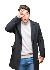 Wall Mural - Young elegant man wearing winter coat over isolated background doing ok gesture shocked with surprised face, eye looking through fingers. Unbelieving expression.