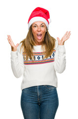 Poster - Middle age adult woman wearing winter sweater and chrismat hat over isolated background celebrating crazy and amazed for success with arms raised and open eyes screaming excited. Winner concept