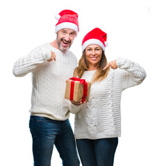 Poster - Middle age hispanic couple wearing christmas hat and holding gift over isolated background with surprise face pointing finger to himself