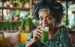 © imagineRbc - A woman with dark hair and a green headband sits in a cafe, smiling and holding a glass of green smoothie