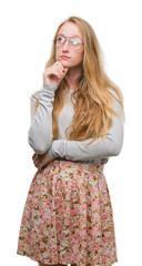 Poster - Blonde teenager woman wearing flowers skirt with hand on chin thinking about question, pensive expression. Smiling with thoughtful face. Doubt concept.