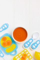 Wall Mural - Carrot puree in a bowl and toy plastic utensils. Baby food concept. Top View. Copy space