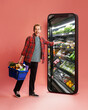 © master1305 - Man in casual clothes, holding grocery basket, reaching into huge smartphone screen showing store against pink background. Convenient food service. Online shopping, food, delivery service, app concept