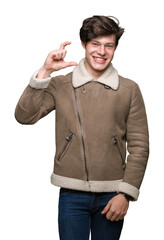 Sticker - Young handsome man wearing winter coat over isolated background smiling and confident gesturing with hand doing size sign with fingers while looking and the camera. Measure concept.