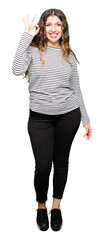 Wall Mural - Young beautiful woman wearing stripes sweater smiling positive doing ok sign with hand and fingers. Successful expression.