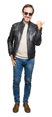 Poster - Middle age handsome man wearing sunglasses and black leather jacket smiling with happy face looking and pointing to the side with thumb up.