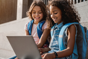 two happy elementary middle school girls friends pupils classmates using laptop gadgets looking on s