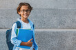 © InsideCreativeHouse - Portrait of happy caucasian young preteen boy elementary middle school pupil in eyeglasses with backpack holding notebook books outside the primary school. Education concept copy space