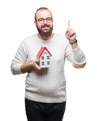 Sticker - Young caucasian real state agent man holding house isolated background surprised with an idea or question pointing finger with happy face, number one