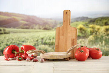 Canvas Print - Empty wooden cutting board on and wooden table background with copy space for food and products. Image for montage objects display. Green ladscape of big green garden fields in distance.