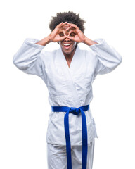 Wall Mural - Afro american man wearing karate kimono over isolated background doing ok gesture like binoculars sticking tongue out, eyes looking through fingers. Crazy expression.