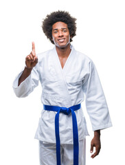 Canvas Print - Afro american man wearing karate kimono over isolated background showing and pointing up with finger number one while smiling confident and happy.