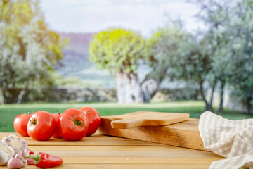 Wall Mural - Wooden table with red tomatoes  with green fields on countryside background. Copy space for products. Vegetables concept and spring and summer time.