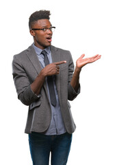 Wall Mural - Young african american business man over isolated background amazed and smiling to the camera while presenting with hand and pointing with finger.