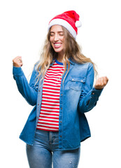 Poster - Beautiful young blonde woman wearing christmas hat over isolated background very happy and excited doing winner gesture with arms raised, smiling and screaming for success. Celebration concept.