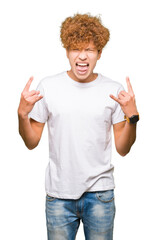 Wall Mural - Young handsome man with afro hair wearing casual white t-shirt shouting with crazy expression doing rock symbol with hands up. Music star. Heavy concept.