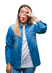 Canvas Print - Young beautiful woman over wearing glasses over isolated background doing ok gesture shocked with surprised face, eye looking through fingers. Unbelieving expression.