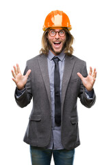 Canvas Print - Young handsome architec man with long hair wearing safety helmet over isolated background celebrating crazy and amazed for success with arms raised and open eyes screaming excited. Winner concept