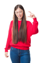 Wall Mural - Young Chinese woman over isolated background wearing glasses smiling and confident gesturing with hand doing size sign with fingers while looking and the camera. Measure concept.