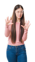 Canvas Print - Young Chinese woman over isolated background wearing glasses afraid and terrified with fear expression stop gesture with hands, shouting in shock. Panic concept.