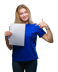 Poster - Young caucasian woman holding blank paper sheet over isolated background with surprise face pointing finger to himself