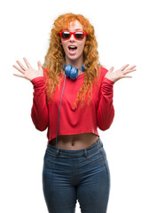 Poster - Young redhead woman wearing headphones very happy and excited, winner expression celebrating victory screaming with big smile and raised hands