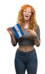 Sticker - Young redhead woman holding flag of Argentina very happy pointing with hand and finger